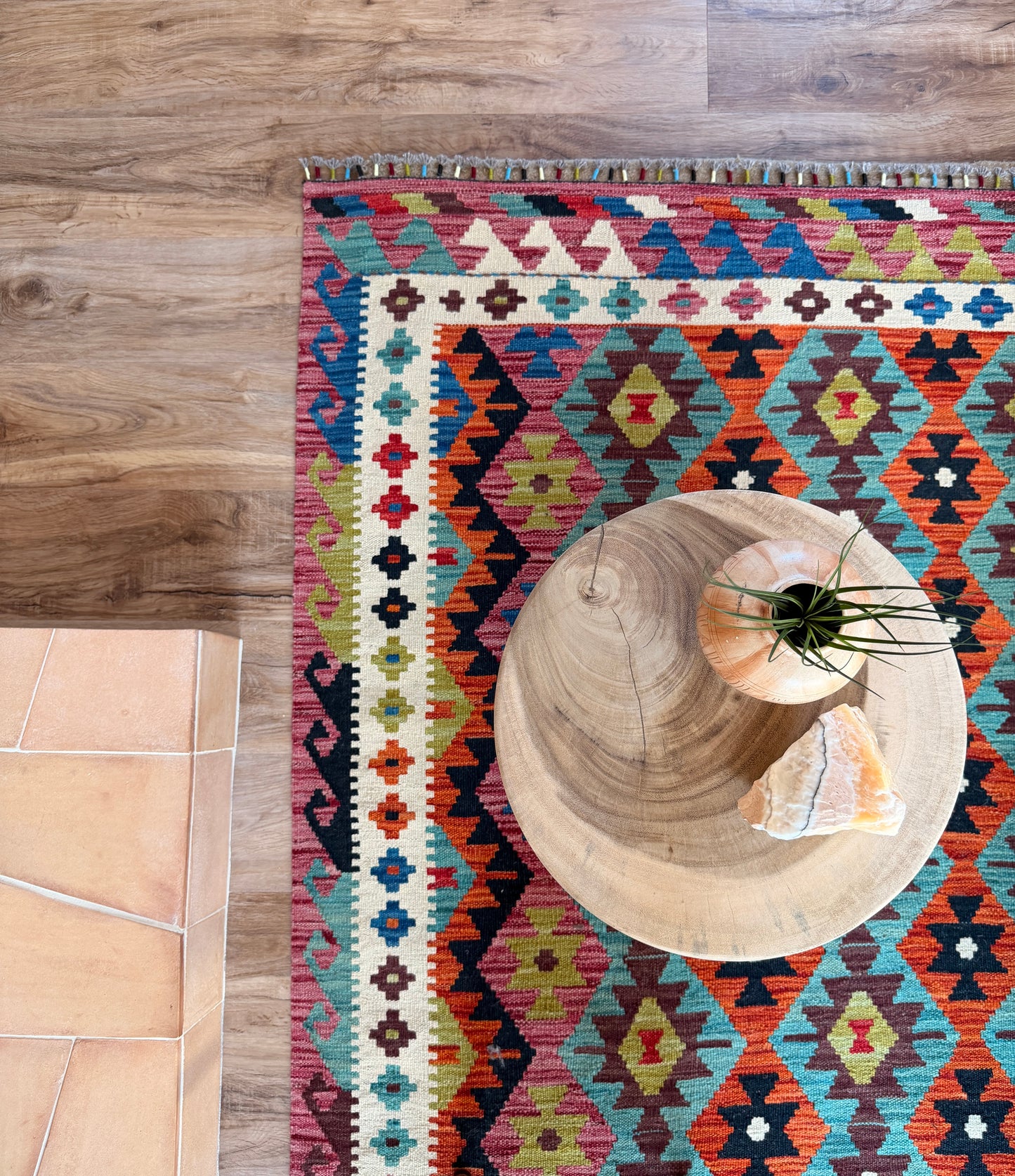 Colorful patterned rug on a wooden floor with a round wooden table and plant.