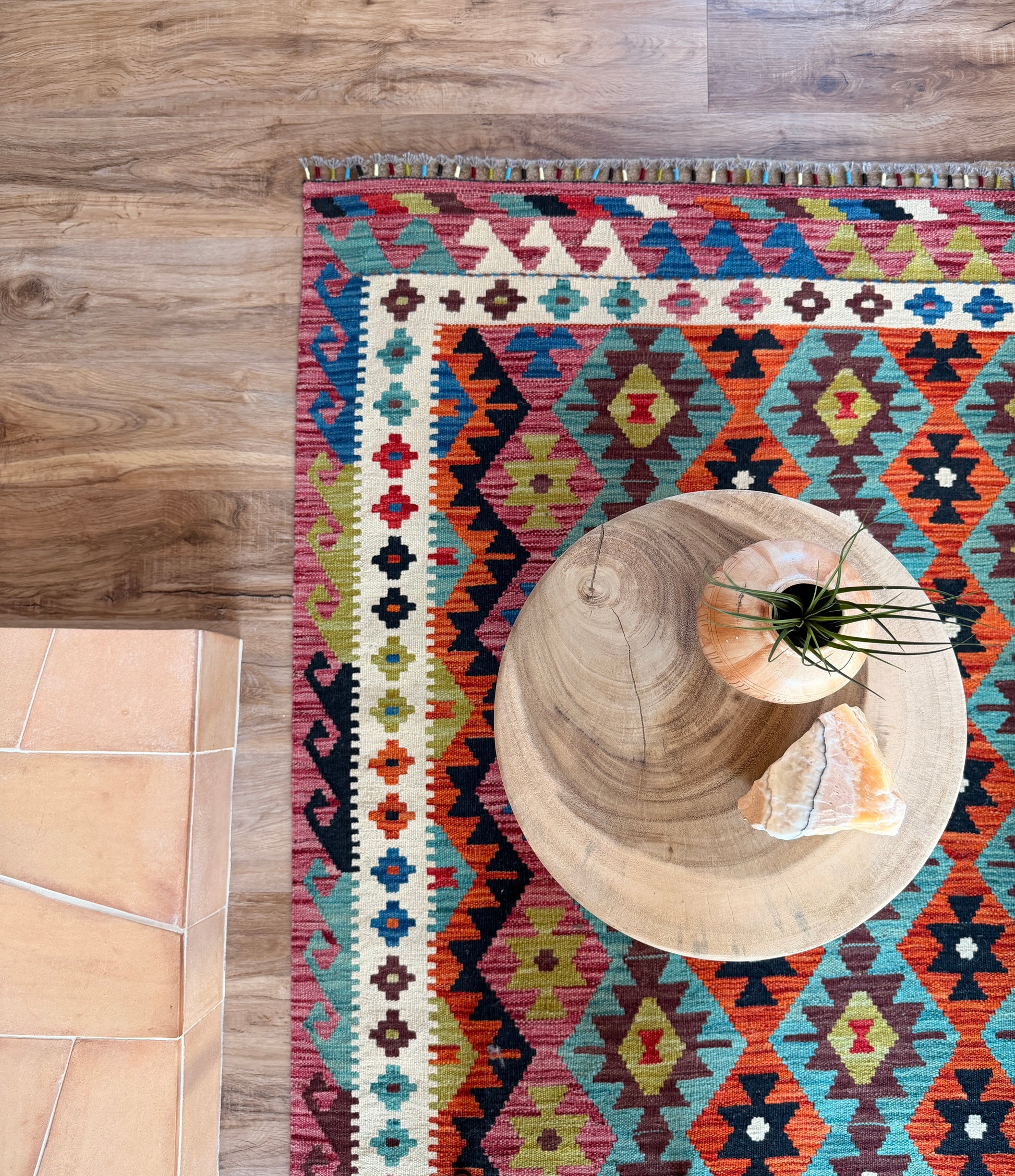 Colorful patterned rug on a wooden floor with a round wooden table and plant.