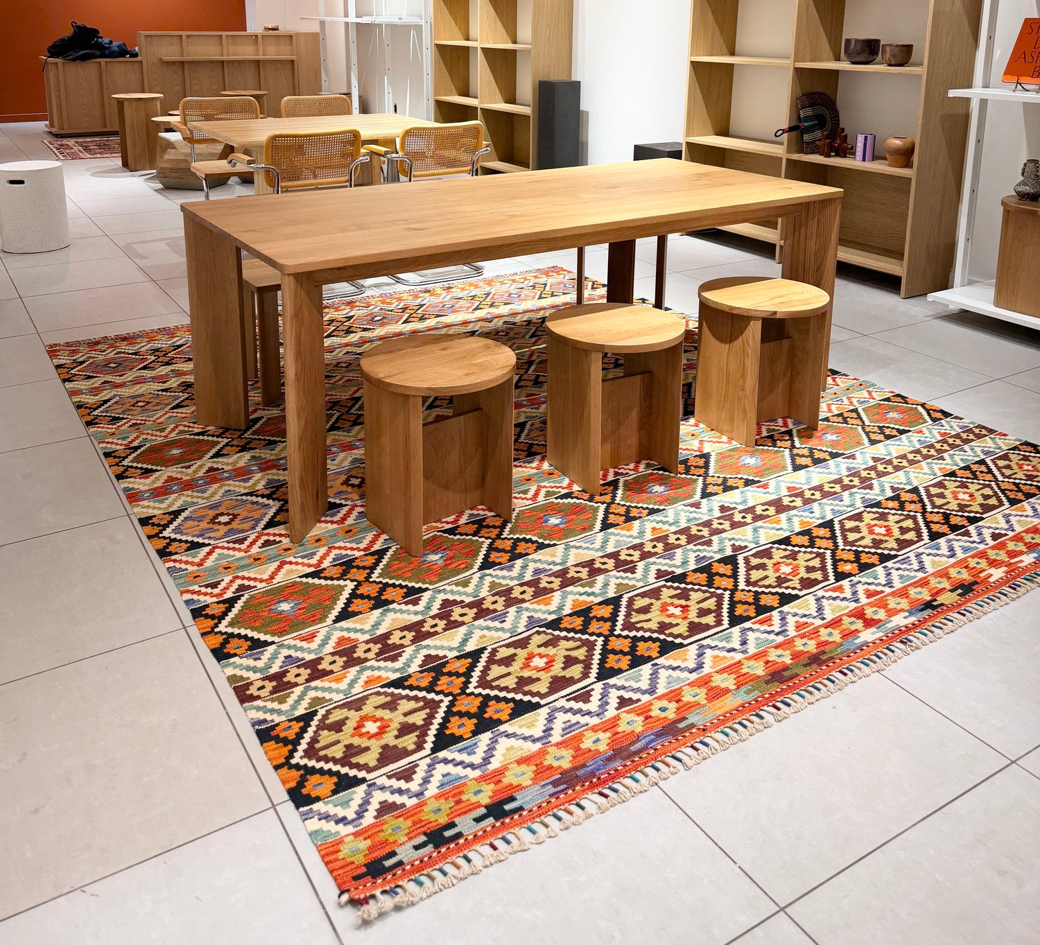 Wooden dining table with stools on a patterned rug in a home decor store with furniture.